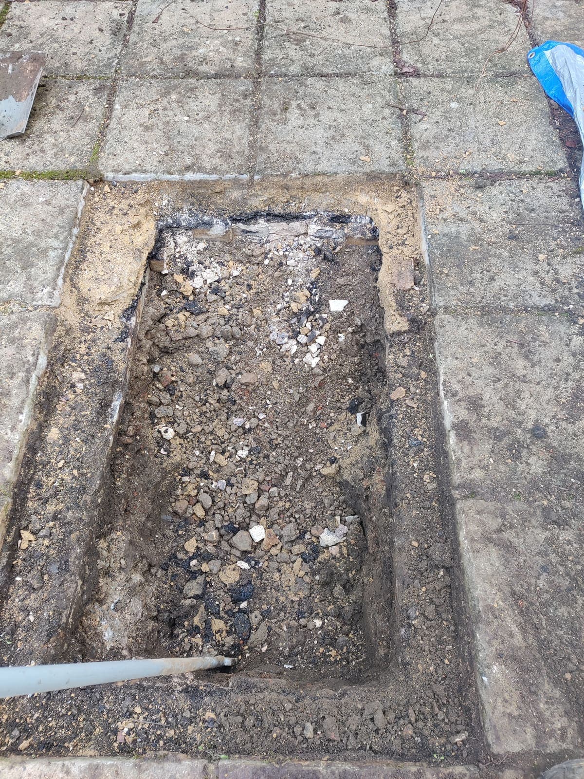 Neat hand-dug excavation through paving slabs, edges cut square and slabs set aside for re-laying