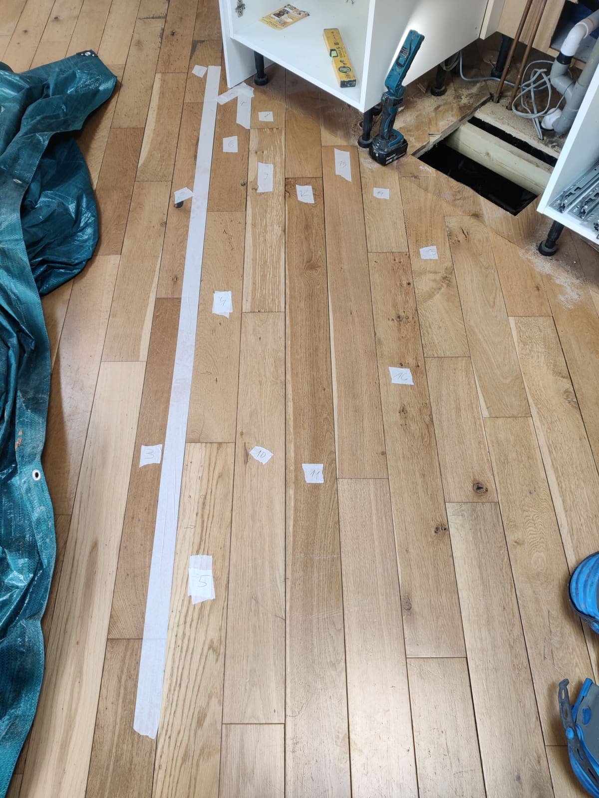 Internal drain repair with oak floorboards lifted, each board numbered with tape for exact reinstatement