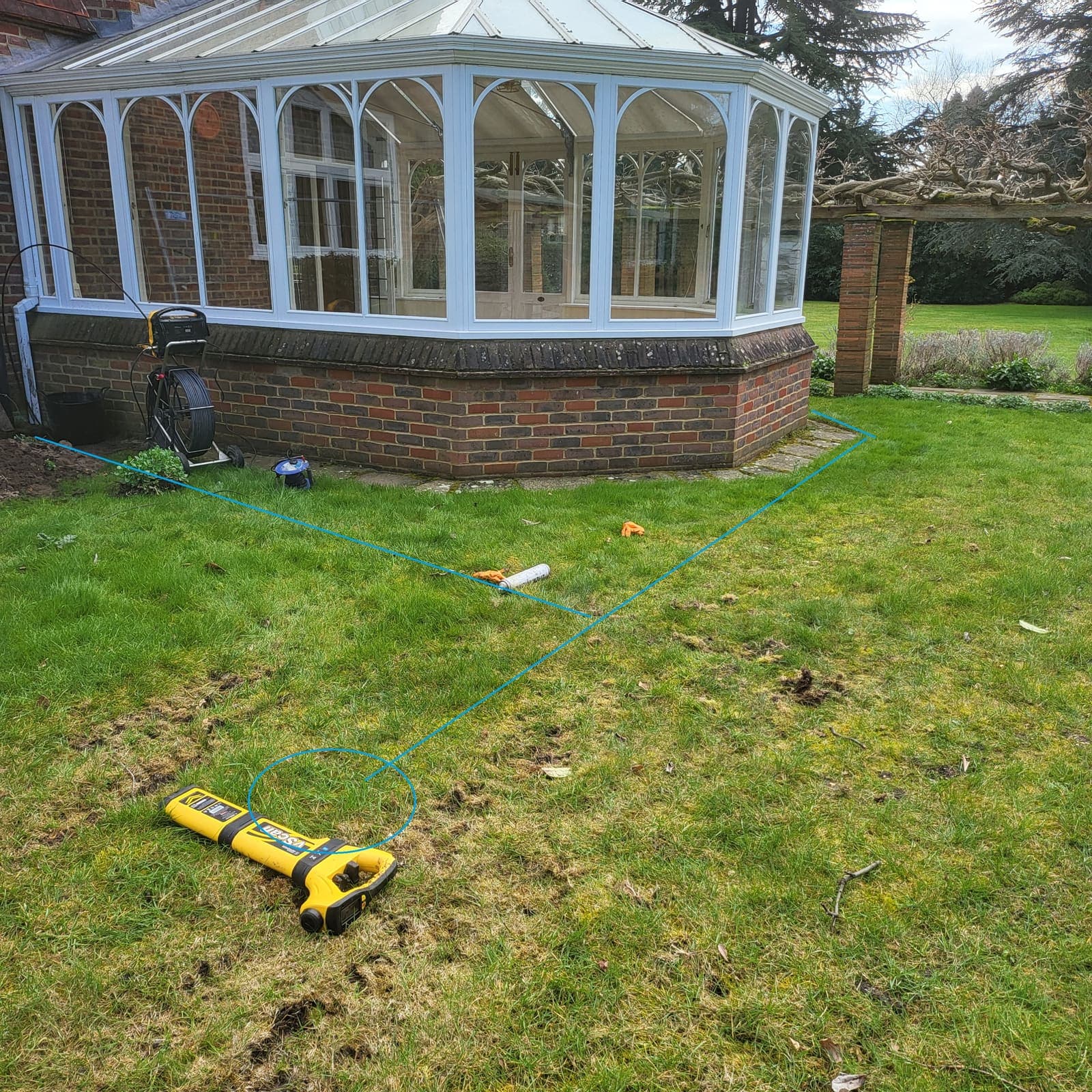 Drain run traced and marked out across a garden during a pre-purchase survey, with the locator and camera reel in shot